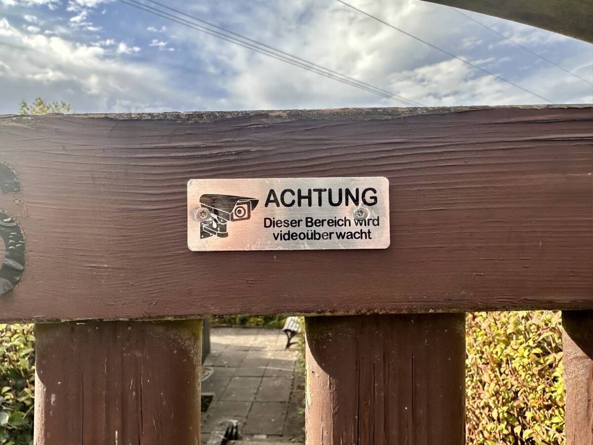 Hinweisschild zur Videoüberwachung als Abschreckung gegen Einbrüche im Kleingarten Warnschild mit Kamera-Symbol und Aufschrift „Achtung! Grundstück wird videoüberwacht!“ am Zaun